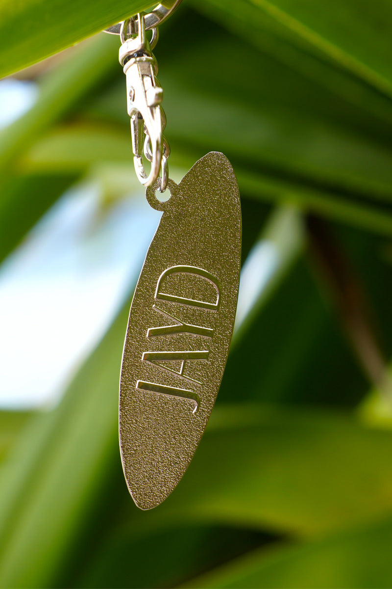 Gold keychain with &#39;JAYD&#39; engraving against a green leafy background