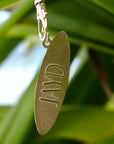 Gold keychain with 'JAYD' engraving against a green leafy background