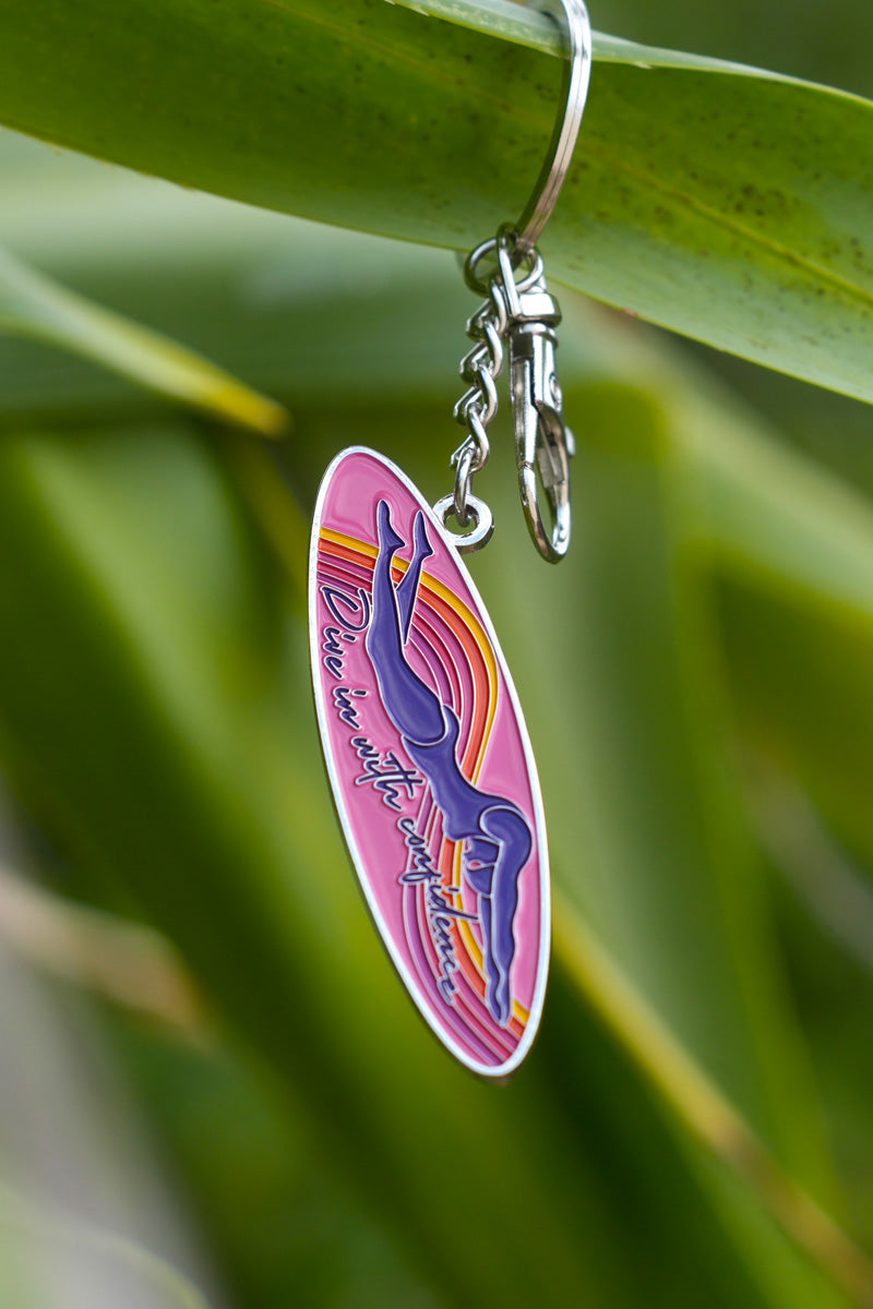 JAYD Swimwear keyring featuring a woman diving into the water with the phrase &#39;dive in with confidence&#39; on a colourful ink surfboard shape.