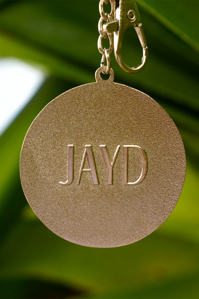 Back of JAYD Swimwear keychain with &#39;JAYD&#39; engraved on a blurred green background