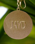 Back of JAYD Swimwear keychain with 'JAYD' engraved on a blurred green background