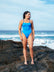 Open water swimmer Madi Armstrong standing on a rock at the beach wearing the JAYD Swimwear Cancun blue one piece swimsuit with contrasting cobalt shoulder straps.
