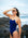 JAYD Swimwear model Molly standing on a beach shading her eyes from the sun, wearing the Lennox one piece swimsuit in navy blue with white shoulder straps and hip cut-outs.