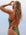 JAYD Swimwear model shown from behind wearing the olive greenLennox one-piece swimsuit with bright pink Vibe shoulder straps and hip cut-out details, photographed outdoors against a pale sky.