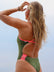 JAYD Swimwear model shown from behind wearing the olive greenLennox one-piece swimsuit with bright pink Vibe shoulder straps and hip cut-out details, photographed outdoors against a pale sky.