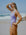 JAYD model Adri wearing the Levanto one piece in Lilac Haze, standing on a beach shading her eyes from the sun.