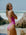 JAYD model Adri standing on a beach looking over her shoulder towards the camera wearing the Levanto one piece in Orchid pink.