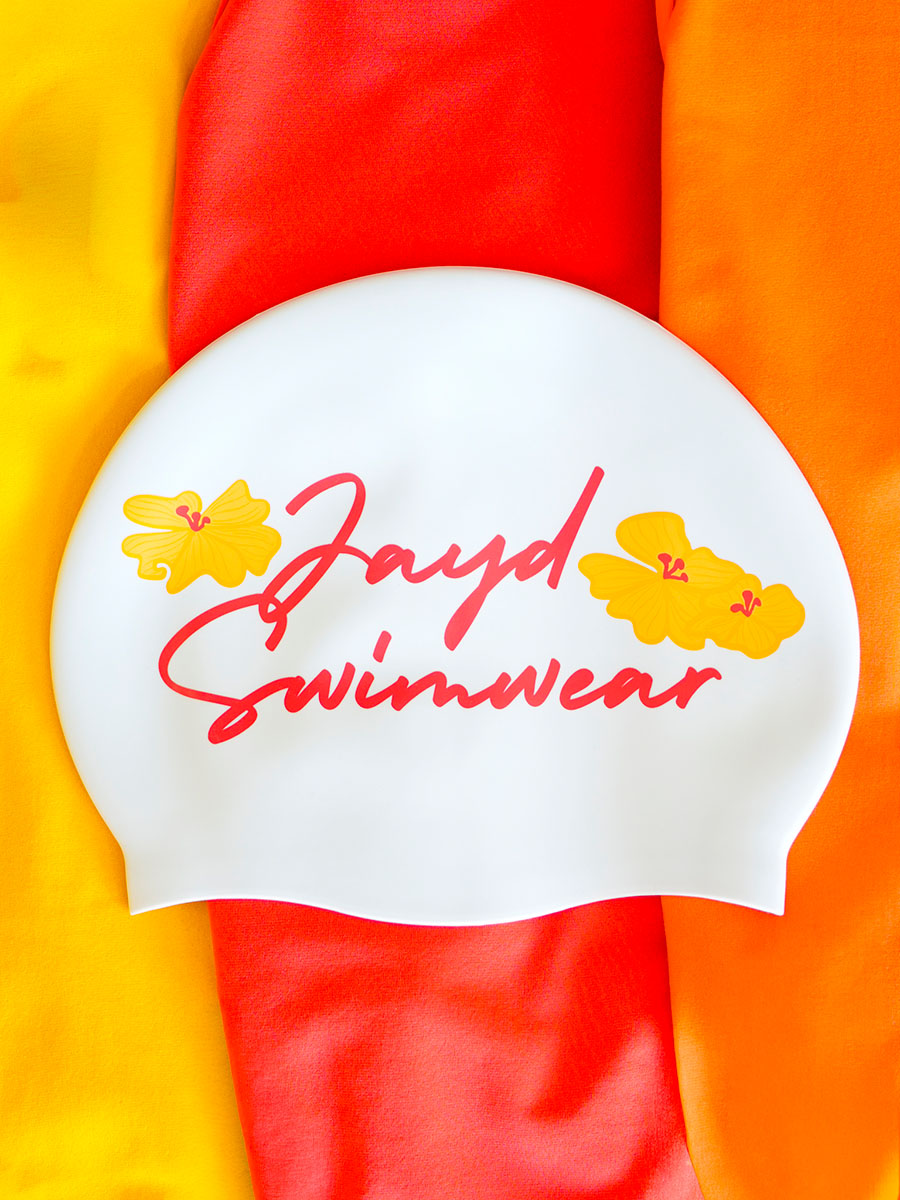 White swim cap with 'Jayd Swimwear' text and floral designs on a colorful background