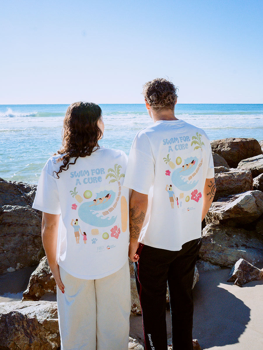 Two people standing on a rocky beach wearing matching t-shirts Swim For A Cure fundraiser t-shirts.