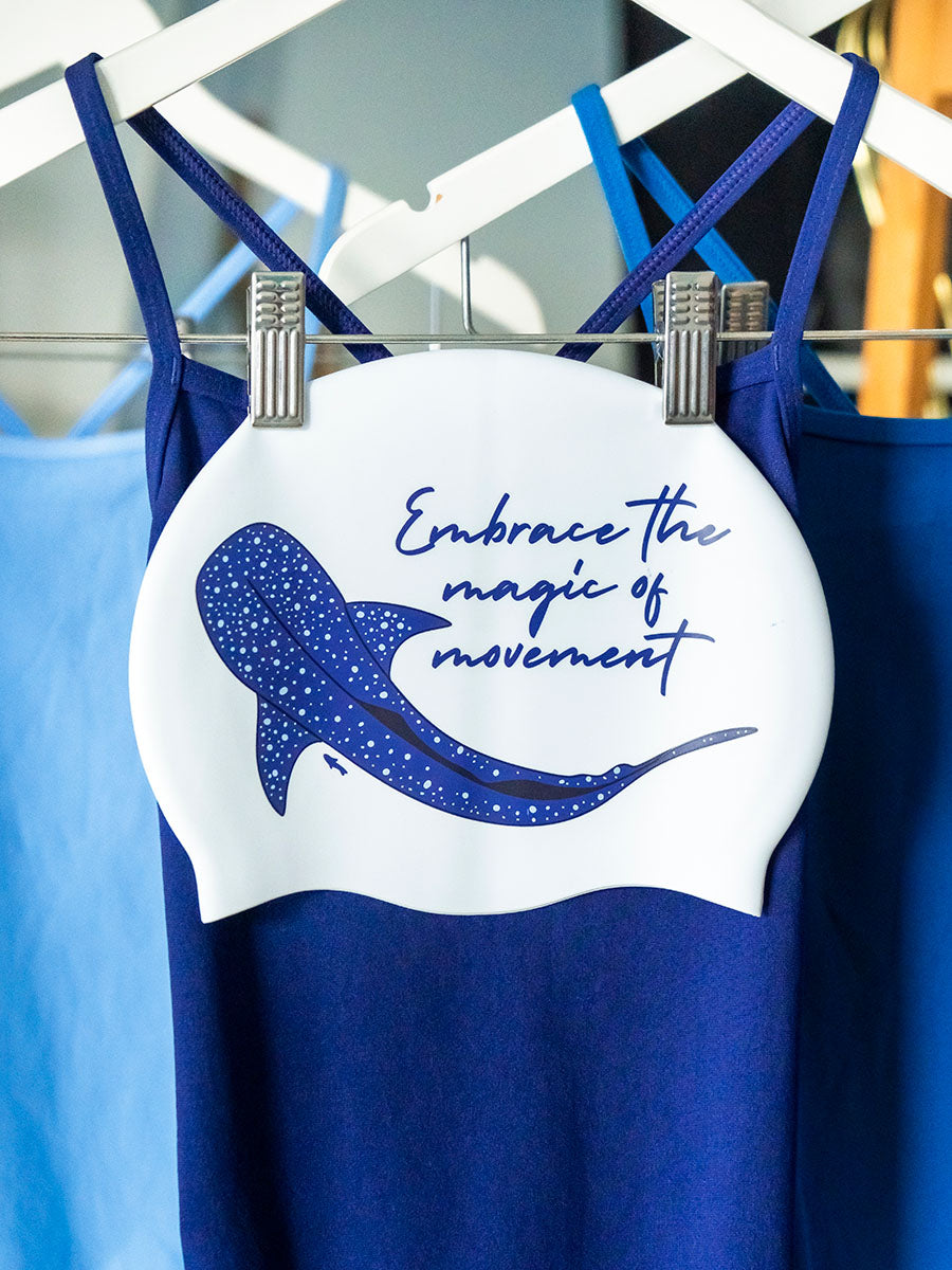 White swim cap with illustration of a whate shark and inspirational text 'embrace the magic of movement'.