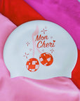 White JAYD swim cap on a pink background with cherry disco balls and text 'Mon Cheri'.