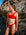 JAYD Triathlete Charlotte Derbyshire standing in front of rocks at a beach wearing the Nalu bikini top in ruby red.
