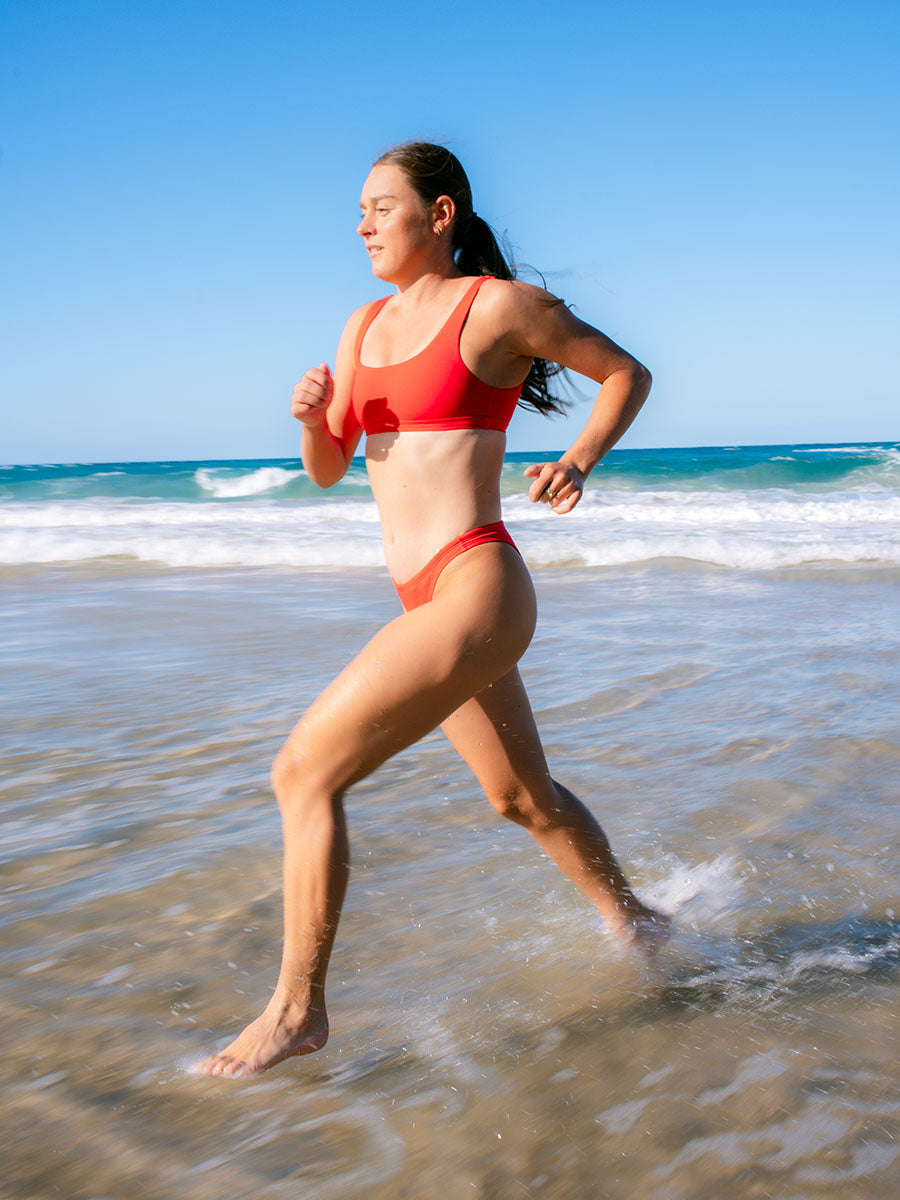 Triathlete Charlotte Derbyshire putting the Nalu Bikini Top to the test as she runs through shallow water along the beach.