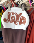 White swim cap with cacao 'JAYD' printed on it, in bold bubble letters, with tropical palm tree & turtle icons hanging on a rack with JAYD Swimwear cacao and cinnamon one pieces.