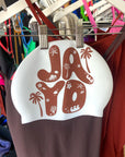 Brown and white swim cap with 'JAYD' design hanging on a rack.