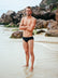 Athlete Wes standing on a rocky beach wearing the JAYD Swimwear men's Ramshark bottoms in black.