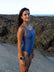 JAYD Swimwear model Ana wearing the Riva one piece in storm blue on a beach with rocks in the distance.