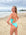 JAYD athlete Emma Woods standing on a beach wearing the Zambia one piece in sea mist blue with contrasting orange shoulder straps.
