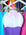 White swimcap with pink hand doing a 'Shaka' signal hanging in front of various JAYD swimsuits.