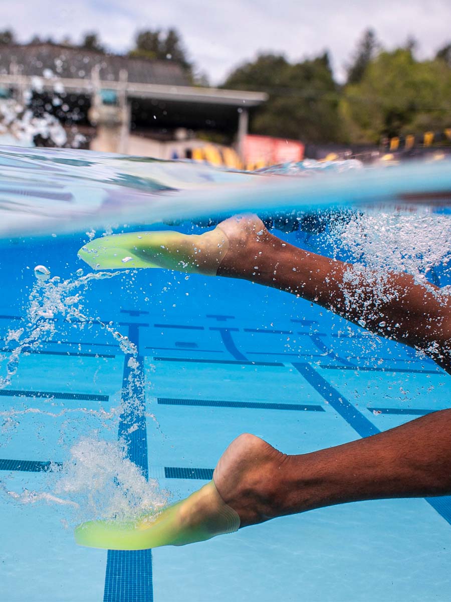 A close-up underwater action shot of a swimmer's legs kicking in a blue pool with bright Volt Green SlipFins from FINIS Swim.