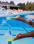 A close-up underwater action shot of a swimmer's legs kicking in a blue pool with bright Volt Green SlipFins from FINIS Swim.