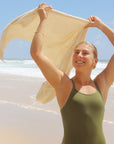 Surf life saving athlete Brodee Trinca waving a towel above her head on the beach, wearing the Soraya JAYD One Piece in olive.