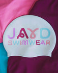 White swim cap with colorful squiggly  text 'JAYD SWIMWEAR' on a multicolored background