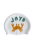 Dive into your next swim with a splash of attitude in this fun double sided JAYD Swim Cap featuring a little orange crab, playfully juggling a cluster of green JAYD Swimwear shells.