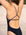 Rear view of JAYD model wearing the black Tallow one-piece swimsuit with secure fixed-back straps, standing outdoors on a sandy beach.