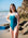 JAYD Swimwear model Amelia standing on a rocky beach wearing the Cove Tallow one piece.