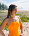JAYD Swimwear model standing on a beach looking into the distance, wearing the Tallow one piece swimsuit in sunshine with a wide chest design for maximum support and comfort.