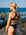 JAYD Swimwear athlete stands on a rocky beach facing the ocean, wearing the black Amalfi bikini bottoms and Vienna top. The photo is taken from behind to show the back of the bikini, which features crisscross straps on the top.