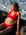 JAYD model wearing a bright red Ruby Vienna bikini top as she sits on dark rocks by the ocean, with waves visible in the background.