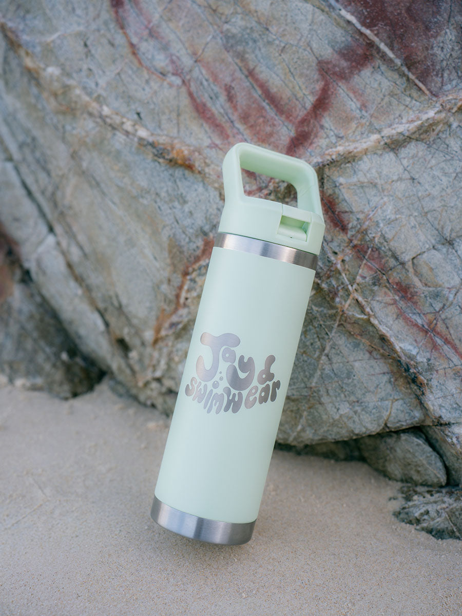 JAYD Swimwear mint green water bottle leaning against a rock at the beach.