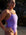 Model Kim wearing the purple lilac haze Zambia one piece swimsuit standing on a beach with large rocks in the background