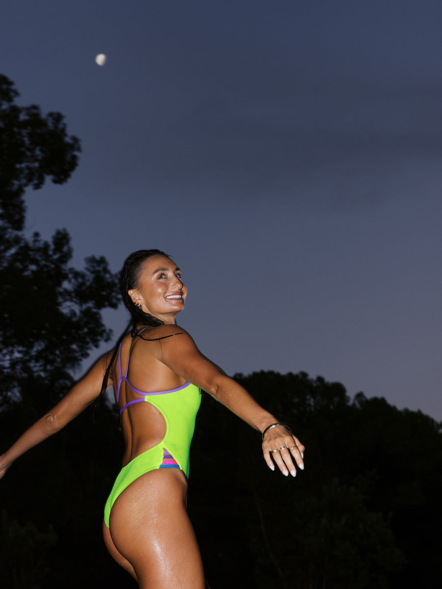 Athlete Lauren Kirwick spinning around under a half moon wearing the JAYD Swimwear Rave Zambia One Piece with Lilac Haze shoulder straps.