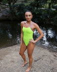 Model Lauren wearing the JAYD Swimwear Zambia Rave x Lilac Haze one piece swimsuit, posing in front of a creek with her hair slicked back from a recent swim.