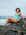 Open water swimmer Madi Armstrong reclining on a rock in front of the ocean wearing the JAYD Swimwear Zambia one piece swimsuit in seamist blue with matcha green straps.