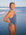 JAYD Swimwear athlete Charlotte Derbyshire wearing the Zambia one piece swimsuit in storm blue with contrasting Seamist shoulder and back straps, stands on a beach with the ocean waves in the background.