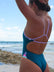 JAYD Swimwear model standing on a beach wearing the Zambia one piece swimsuit in Cove green with purple Lilac Haze straps and multi-coloured hip cut-outs.