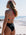 Woman in a contrast Airlie one piece by JAYD swimwear, standing on a beach with ocean view. She is seen wearing the colour black with pink sorbet contrasting straps.