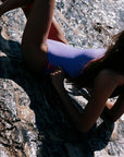 Person sitting on a rock in a lilac haze Lennox one piece. Built for performance