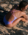 Woman in a lilac haze fixed back one piece sitting on a sandy beach