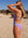 Woman in a JAYD lilac haze and breeze blue IBIZA standing on a beach with rocks in the background.