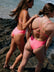 Two women in JAYD swimwear's Vibe coloured one pieces standing on a rocky beach.