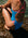 Person wearing a cancun blue and vibe pink fixed back one piece, sitting on rocks by water. One piece is built for performance