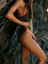 Person wearing an olive green and vibe coloured one piece leaning against a rocky wall.