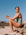 Woman in a matcha green fixed back on piece sitting on a rock at the beach. She is wearing the Zambia style